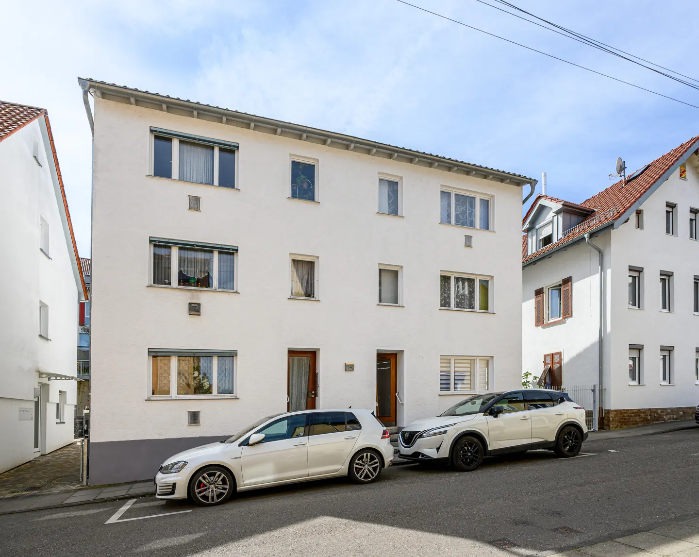 Exterior of a three-story white apartment building with two white cars parked in front.