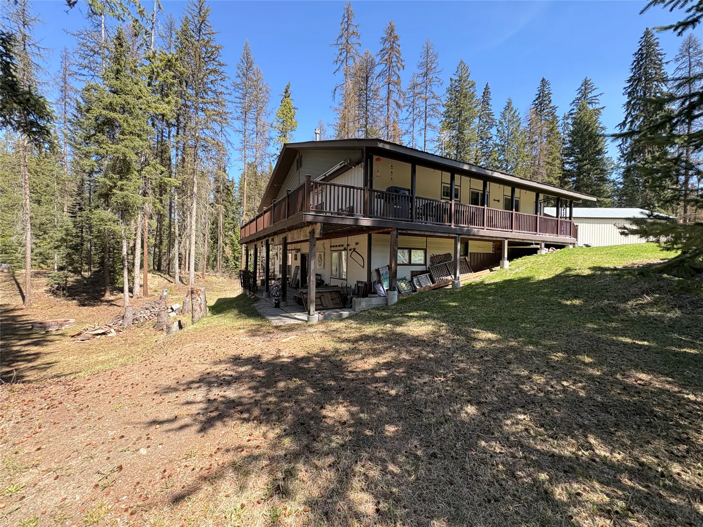 Two-story house with a brown deck, surrounded by tall trees and a grassy lawn.
