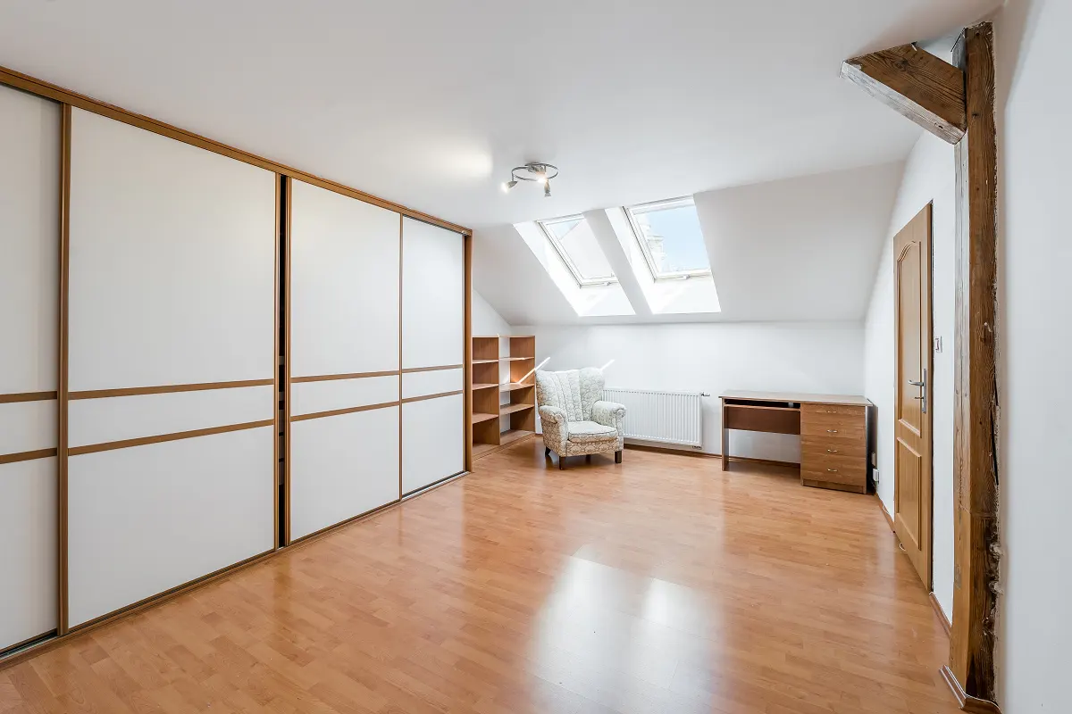 Attic room with wood floors, white walls, and two skylights. A large white closet, desk, and armchair furnish the space.