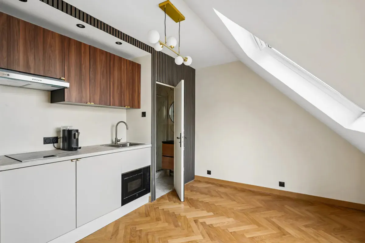 Modern kitchen with wood cabinets, white counters, herringbone floors, and a sloped ceiling with a skylight.