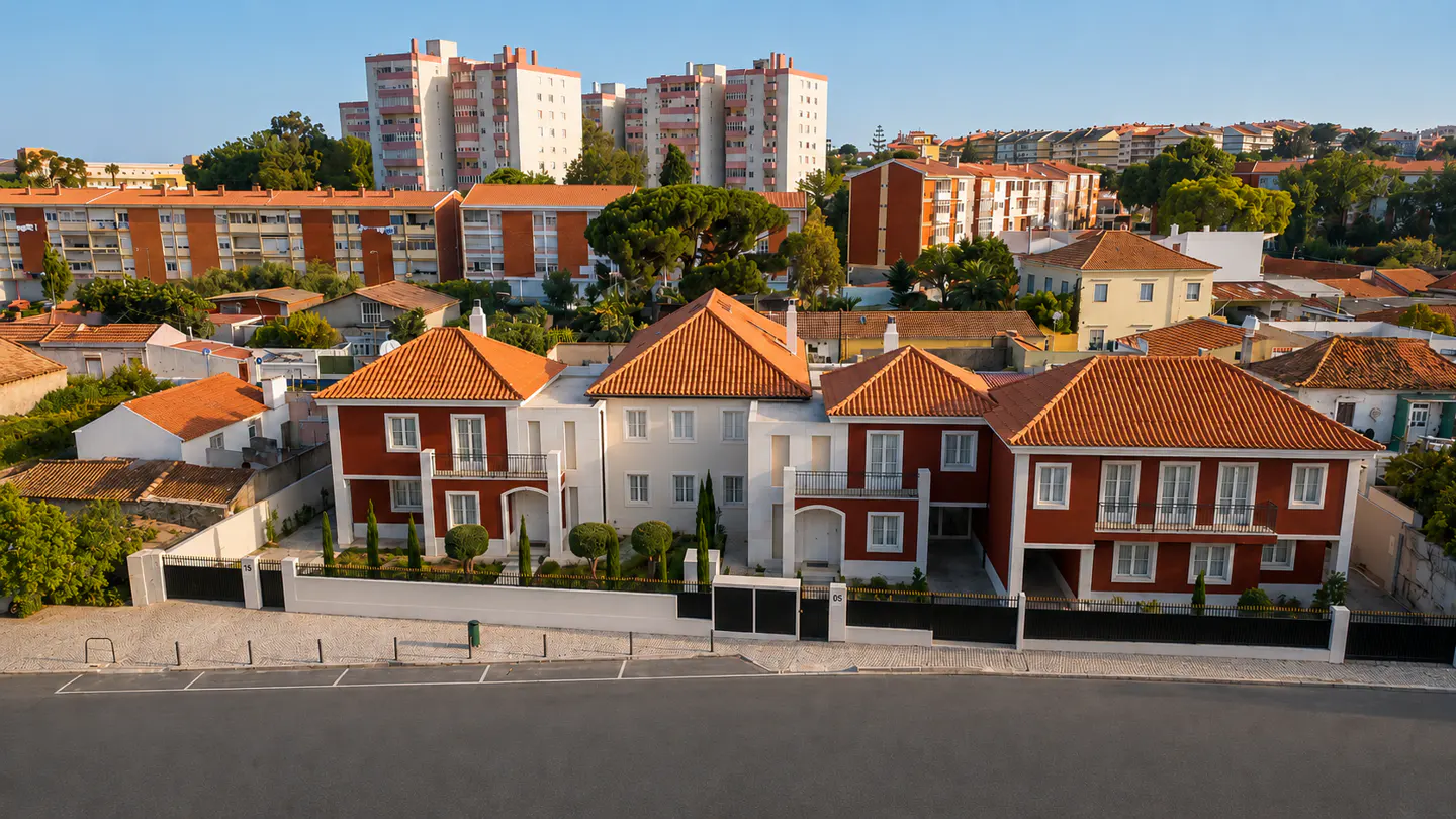 Aerial view of a red and white villa with a tiled roof, surrounded by a residential neighborhood under a clear blue sky.
