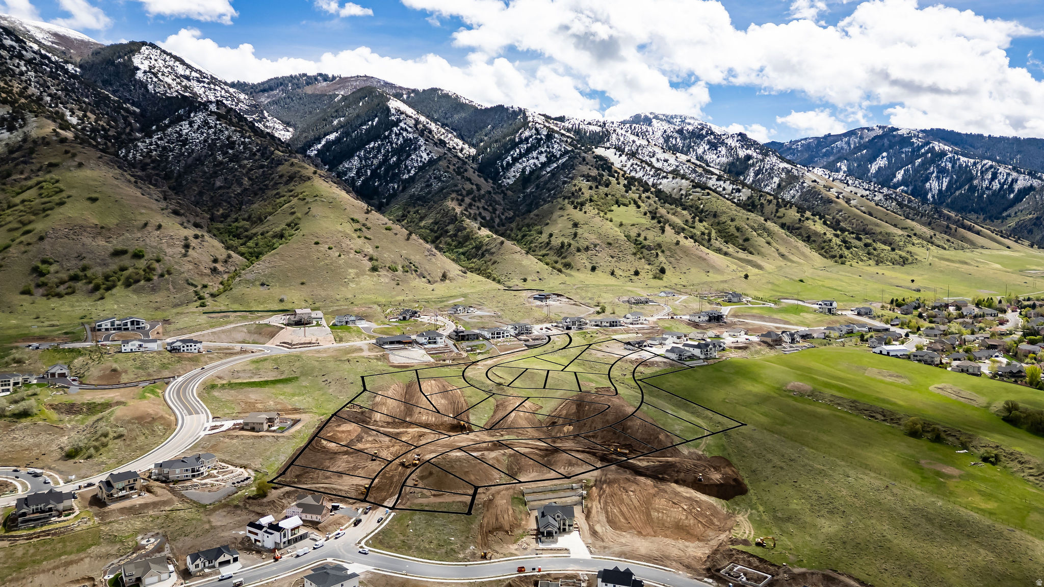 Aerial view of a real estate development with mountain backdrop. New home lots are outlined in black. Some homes are built, others under construction.