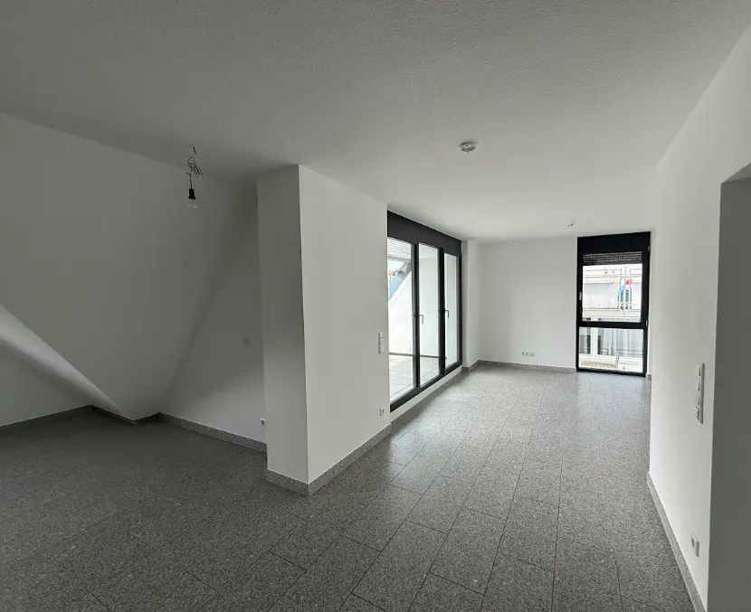 Bright, empty room with gray tile floor, white walls, and black-framed windows. A bare bulb hangs from the ceiling.