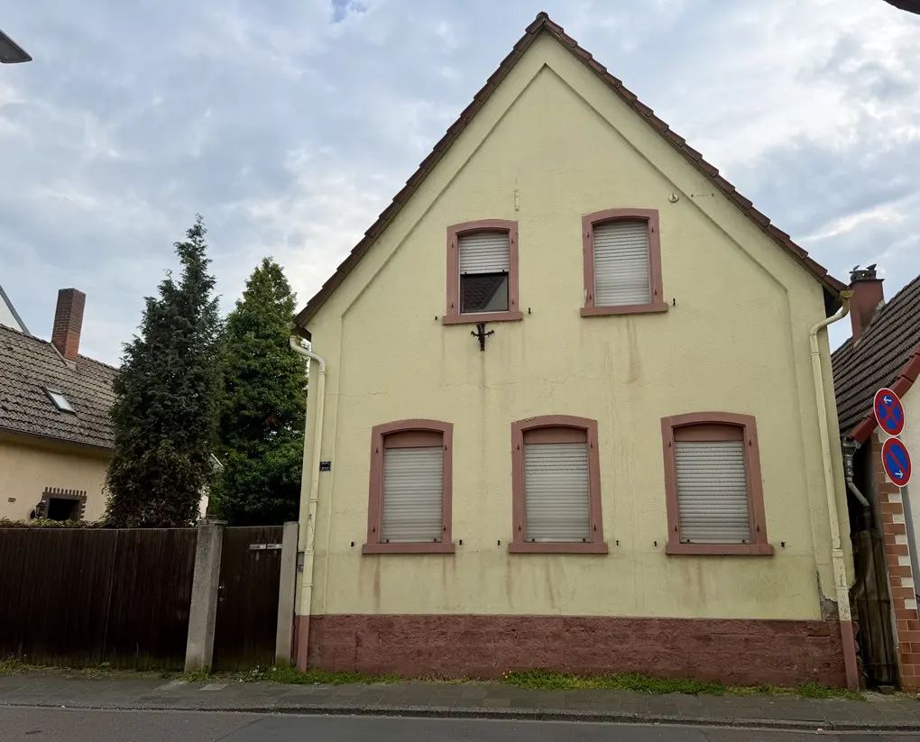 Two-story yellow house with brown trim and a brown roof. The windows have white blinds. There are trees and other houses in the background.
