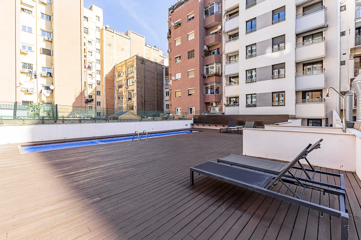 Rooftop pool area with wooden deck, lounge chairs, and city buildings in the background.
