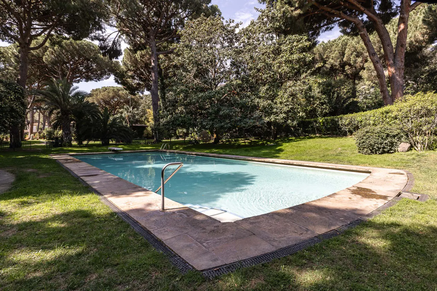 Rectangular swimming pool with stone surround, surrounded by green grass and trees.