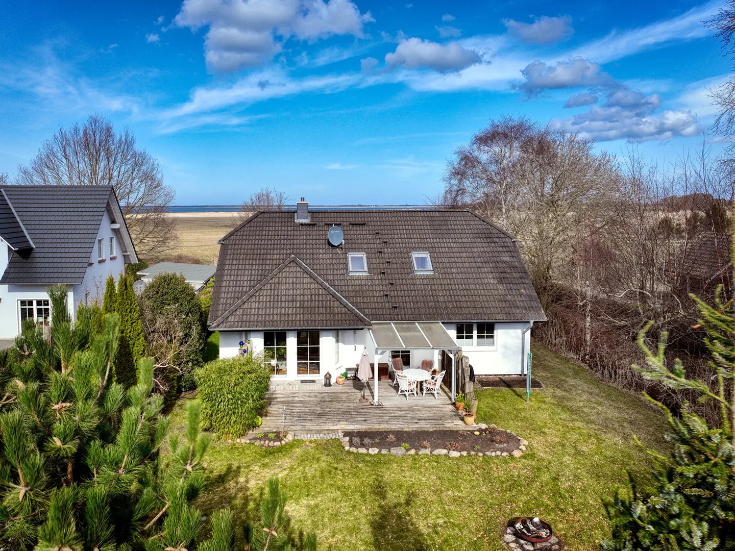 Aerial view of a white house with a brown roof, a wooden deck, and a green lawn under a blue sky.
