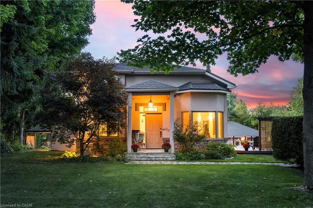 Beige two-story house with a gray roof, front porch, and large front yard at dusk.