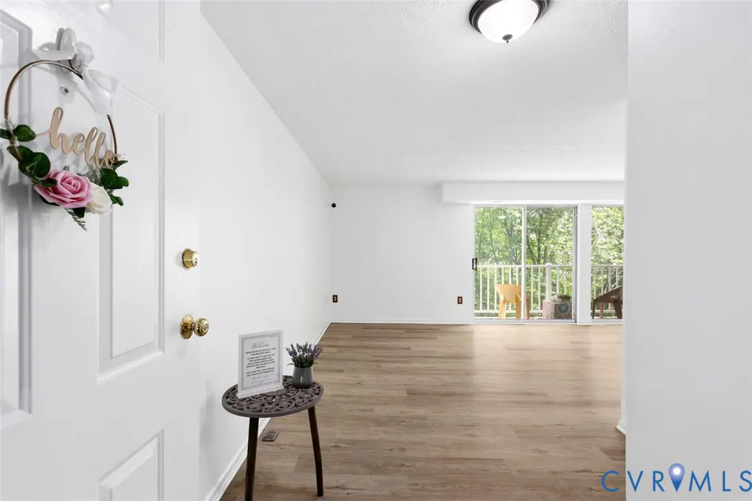 A bright, white entryway with a "hello" wreath on the door. A small table holds a framed sign and lavender. Wood floors lead to a sliding glass door.