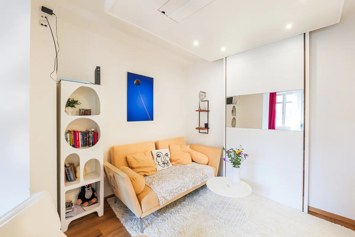 Modern living room with a peach sofa, white arched bookshelf, round coffee table, and a large mirrored sliding closet.