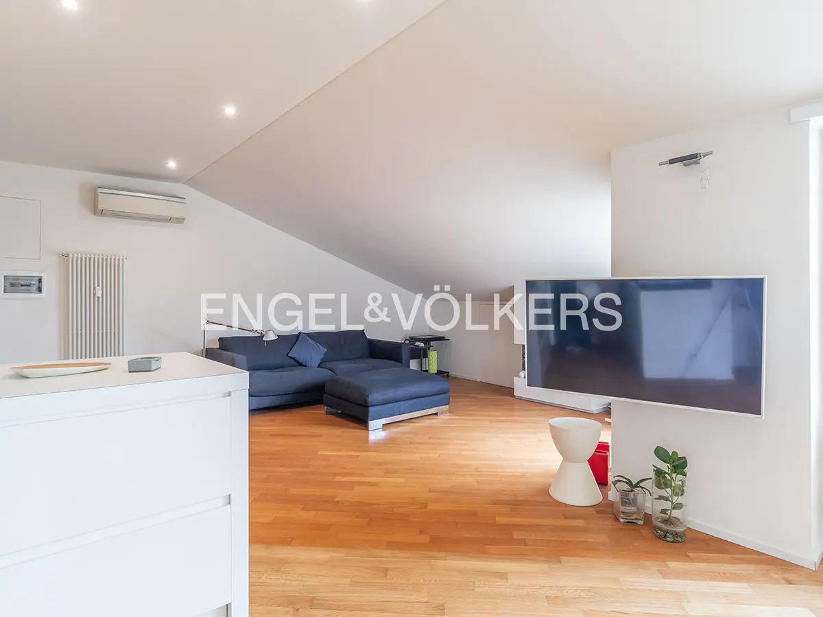 Modern attic living room with hardwood floors, a dark blue sofa, a wall-mounted TV, and white sloped ceilings.