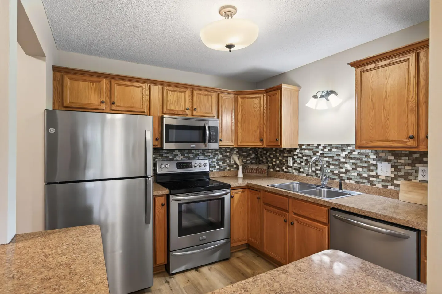 A kitchen with stainless steel appliances, wood cabinets, and mosaic tile backsplash.