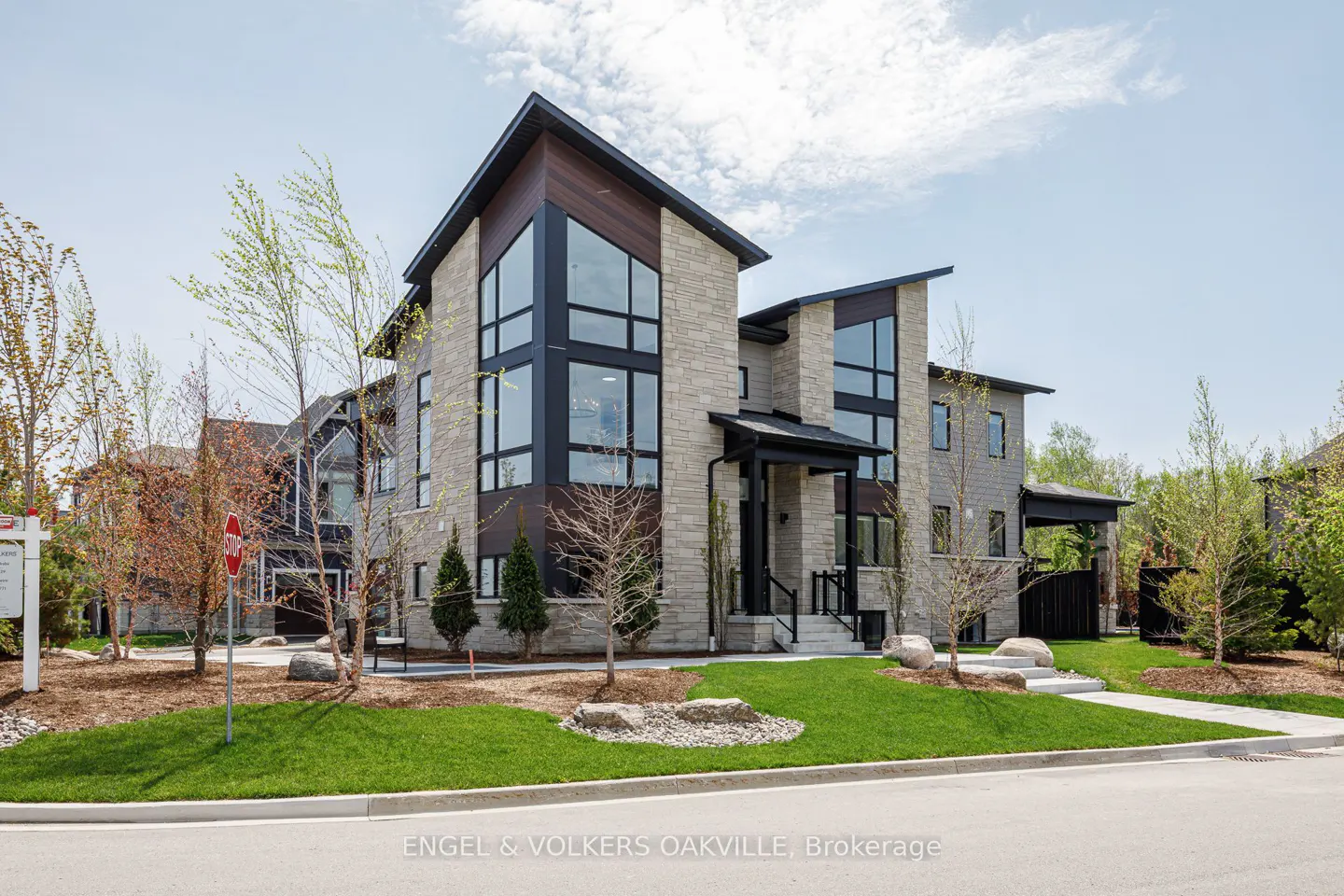 Modern two-story home with stone and wood facade, black window frames, and green lawn on a sunny day.