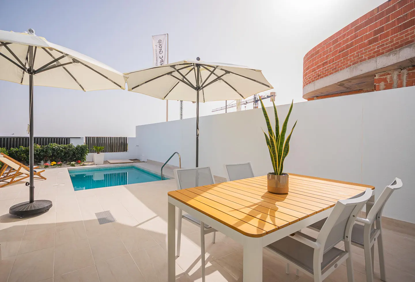 Outdoor patio with a small pool, table, chairs, and umbrellas. A potted plant sits on the table.