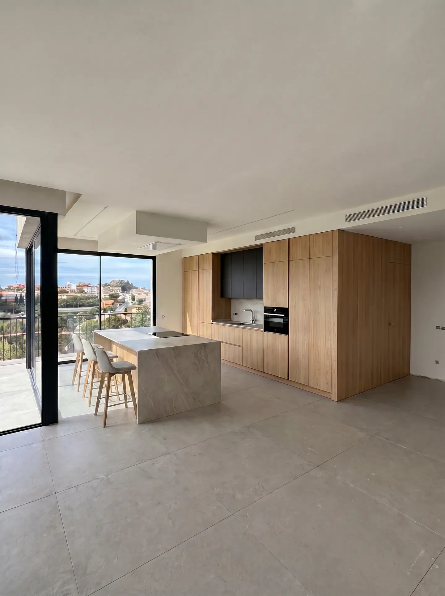 A bright, modern kitchen with a large island, wooden cabinets, and a view from the window.