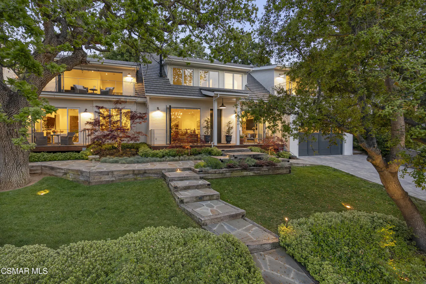 Two-story white house with stone steps leading to the front door, surrounded by green grass and trees.