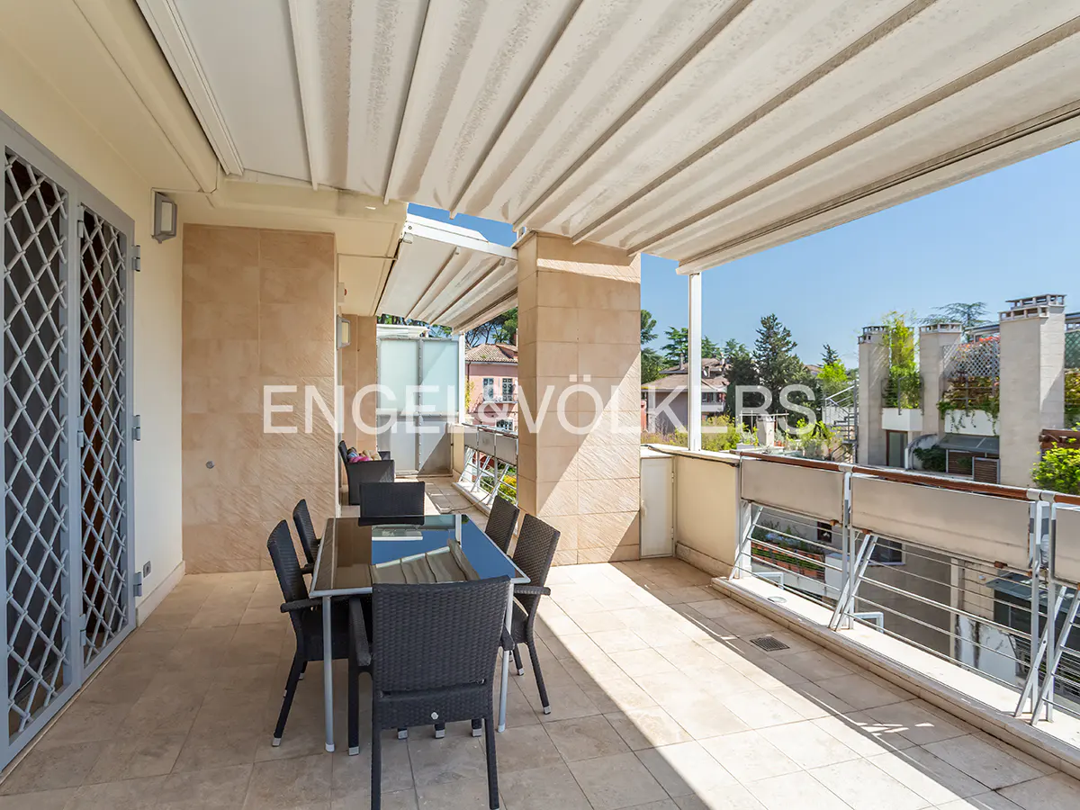 A covered patio with a black table and chairs overlooks a neighborhood on a sunny day.