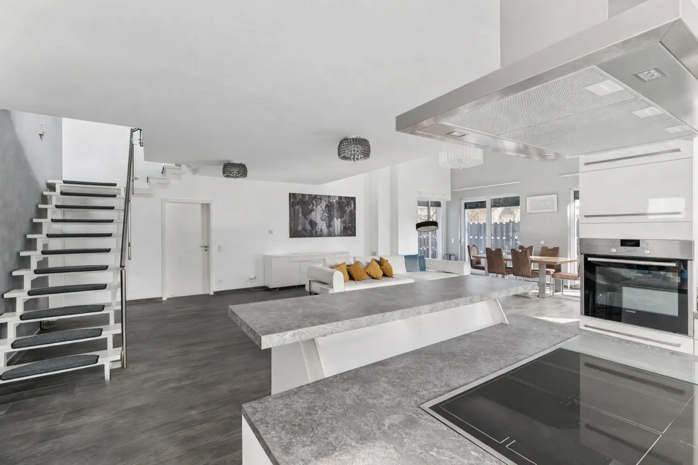 Open-concept home interior with gray floors, white walls, and a modern kitchen island. A staircase leads to the upper level.