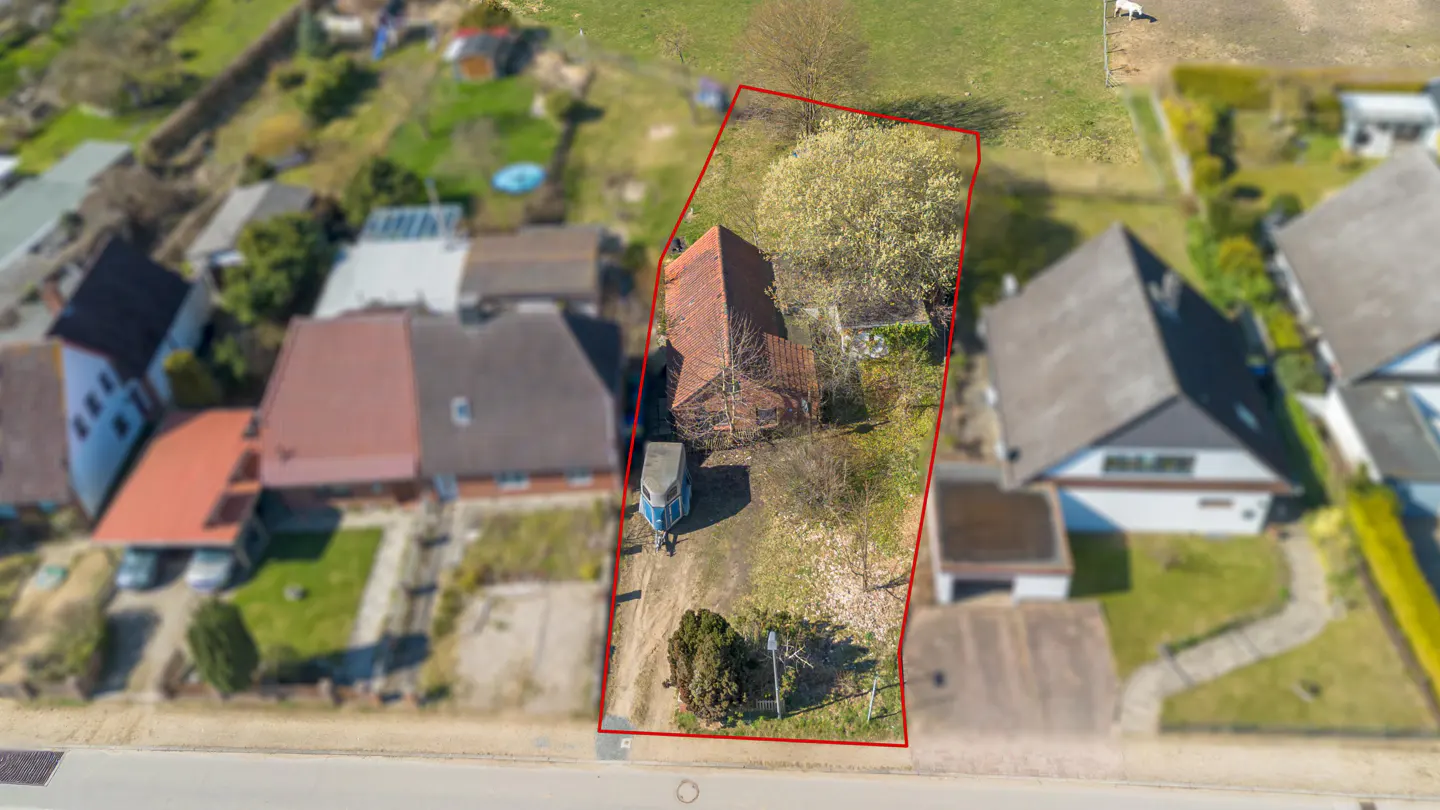 Aerial view of a house with a red roof, surrounded by a red boundary line, indicating property lines. Other houses and greenery are visible.