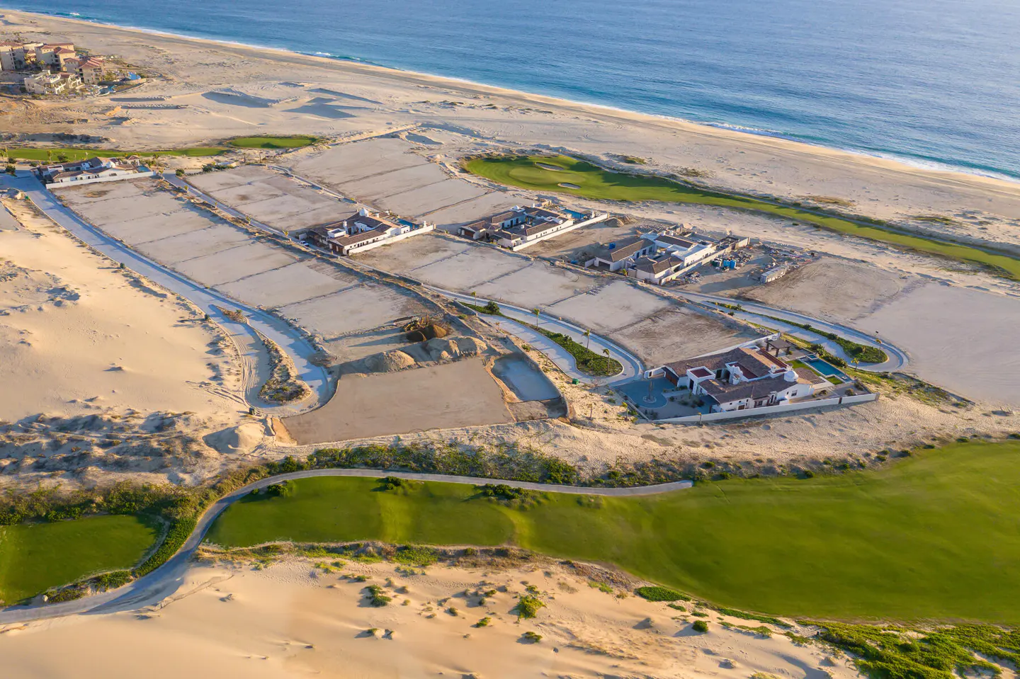 Aerial view of luxury coastal homes under construction near a golf course and sandy beach along the blue ocean.
