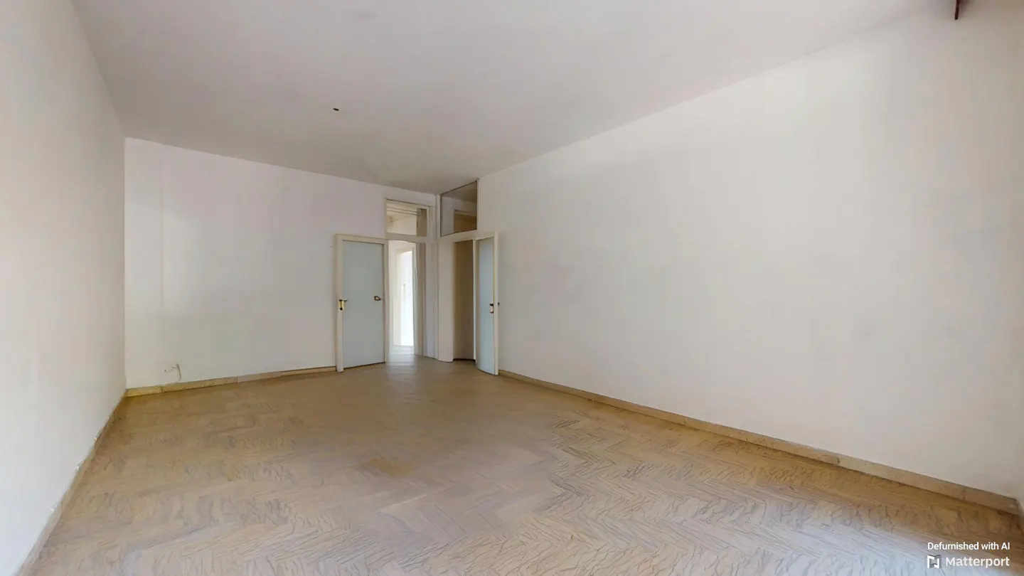 A bright, empty room with white walls and parquet flooring. Two open doorways lead to other rooms.
