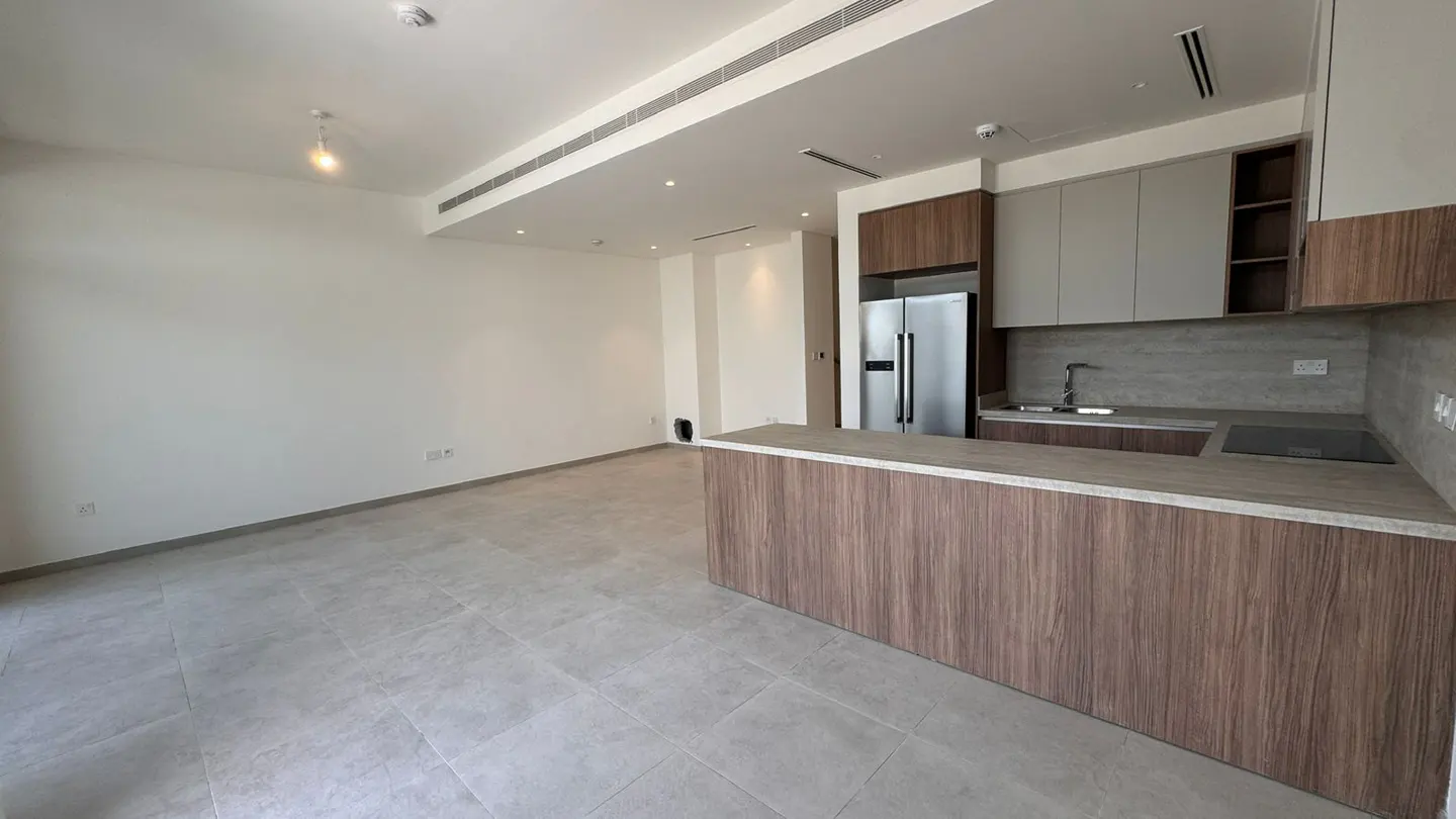 A bright, empty apartment with gray tile floors and a kitchen with wood cabinets and stainless steel appliances.