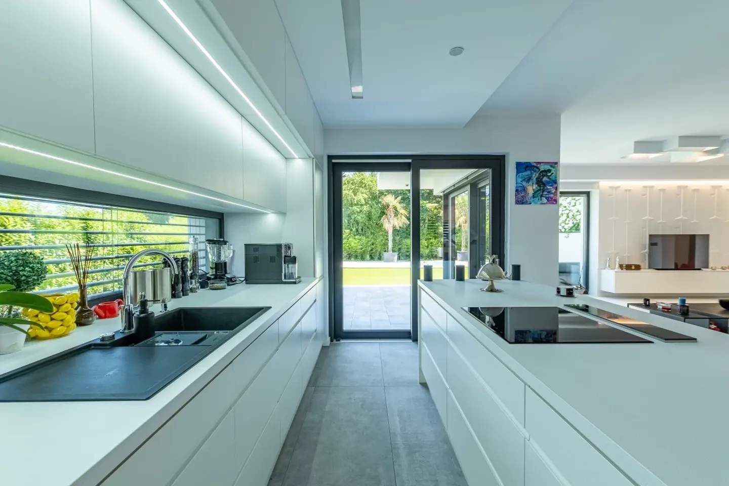 Bright, modern kitchen with white cabinets, black sink, and island. Sliding glass doors lead to a green lawn. Open floor plan to living room.