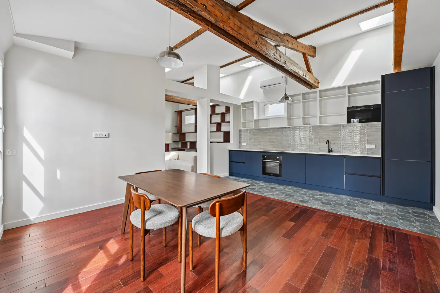 Modern kitchen with navy cabinets, wooden dining table, and exposed ceiling beams over hardwood floors.