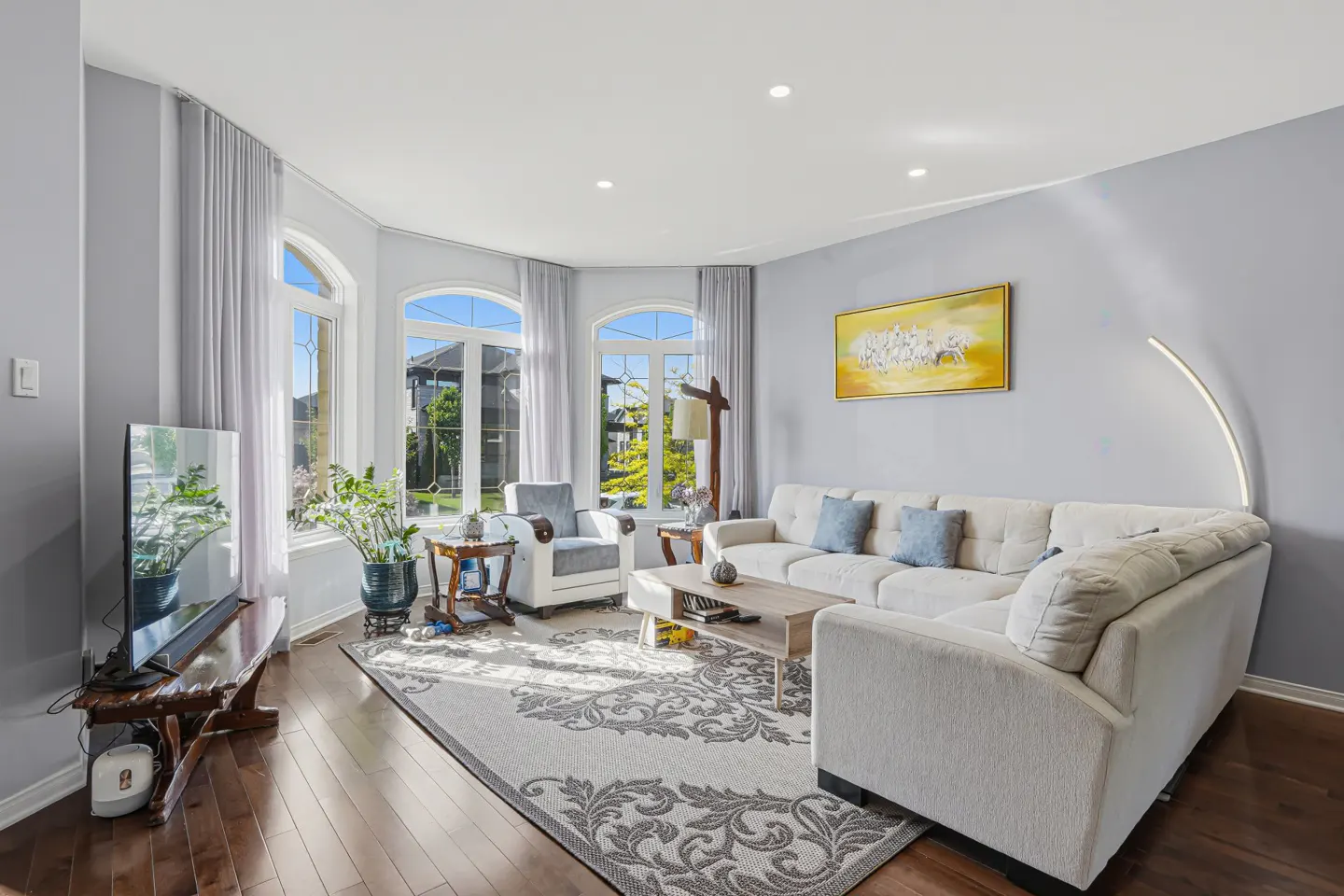 Bright living room with a white sectional sofa, patterned area rug, wooden coffee table, and large arched windows.
