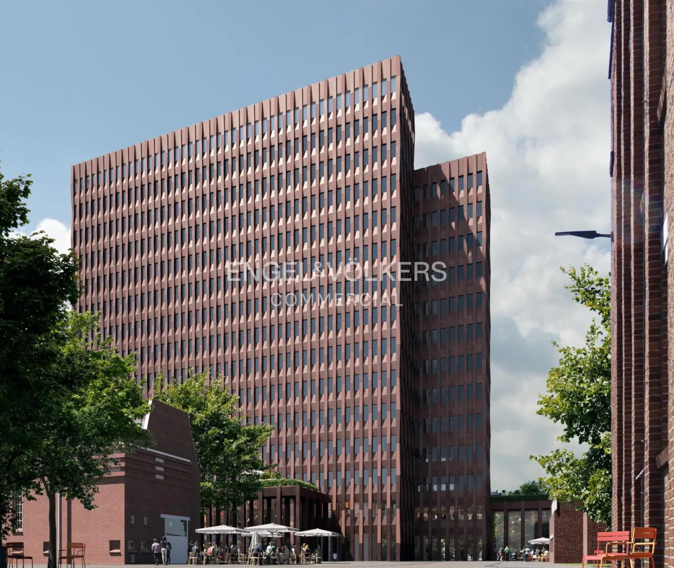 Exterior view of a modern, multi-story brick building with many windows, trees, and people sitting at tables outside.