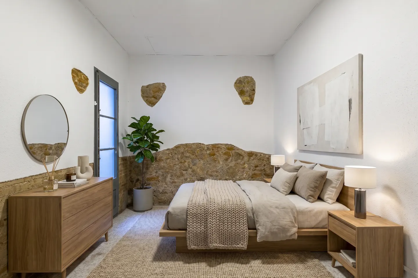 Bedroom with a stone accent wall, a wooden bed, and matching nightstands. A round mirror hangs above a wooden dresser.
