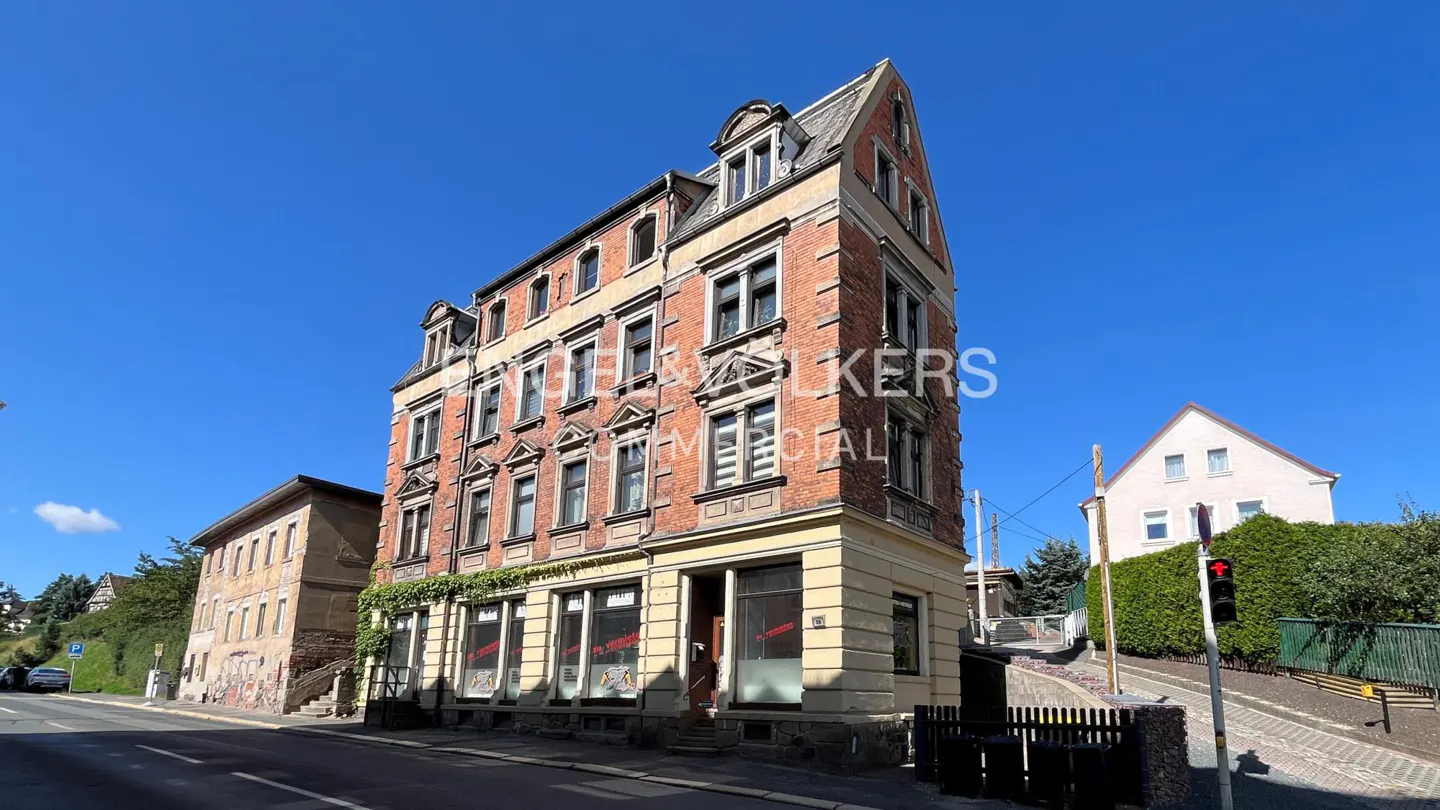 A three-story red brick building with a commercial space on the ground floor under a clear blue sky.