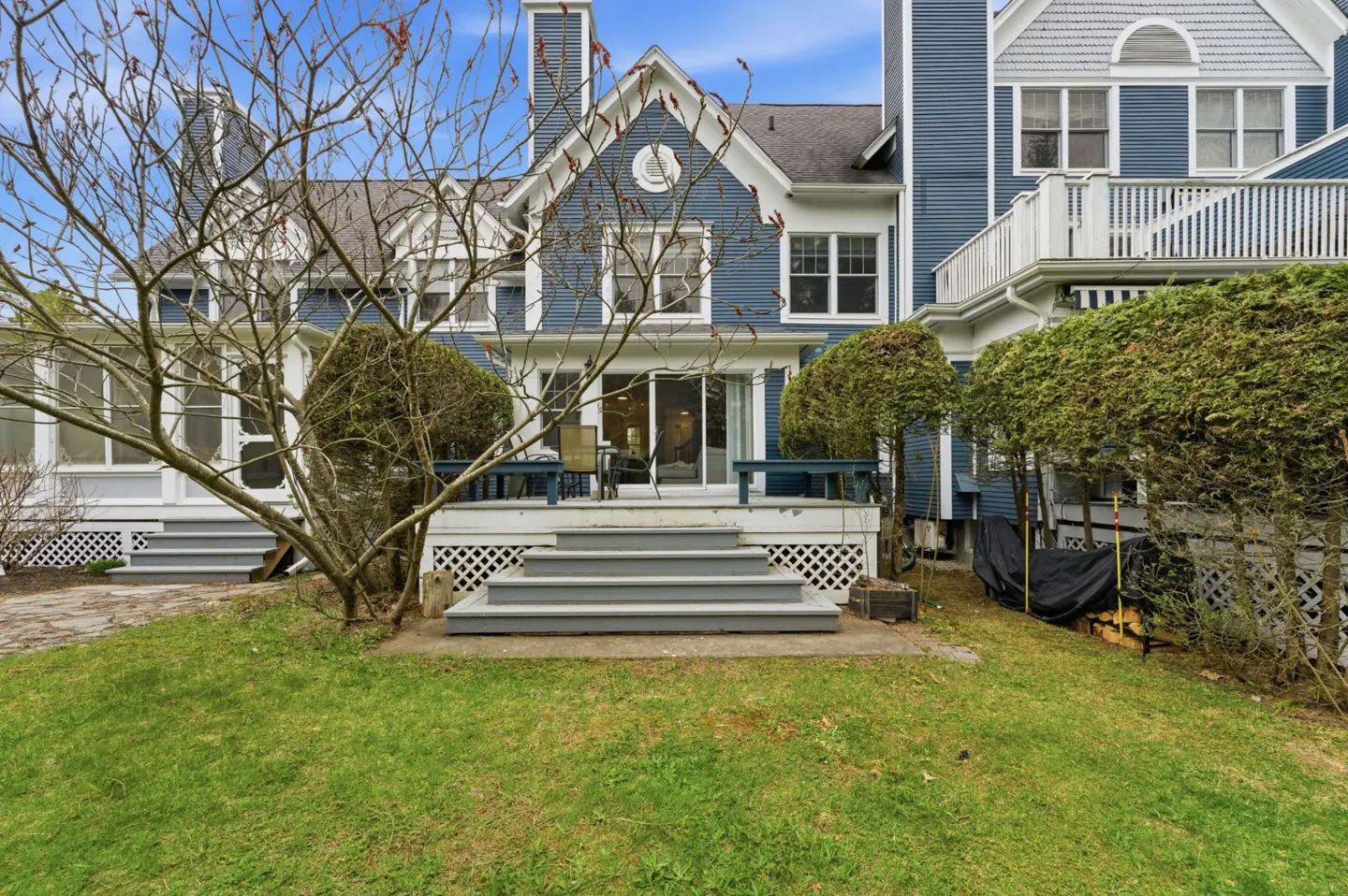 Backyard view of a blue house with white trim, a deck, and a green lawn.