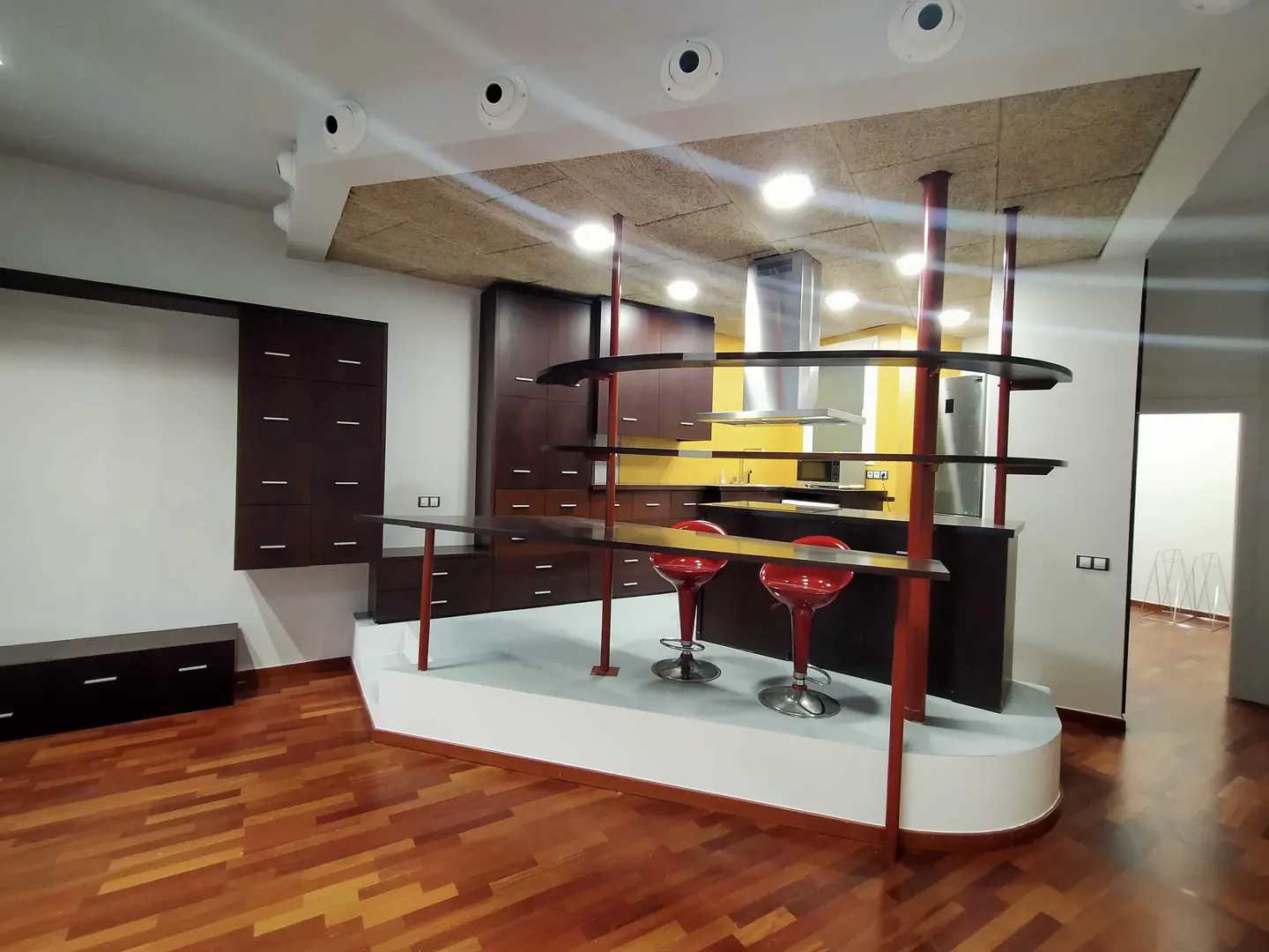 A modern kitchen with wood floors, dark cabinets, and a breakfast bar with red stools.