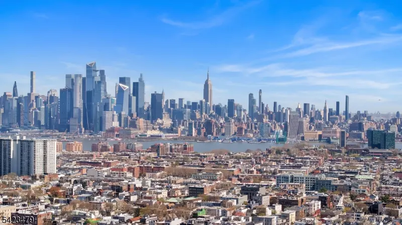 Cityscape view under a blue sky. Buildings and houses fill the foreground, with skyscrapers in the background.