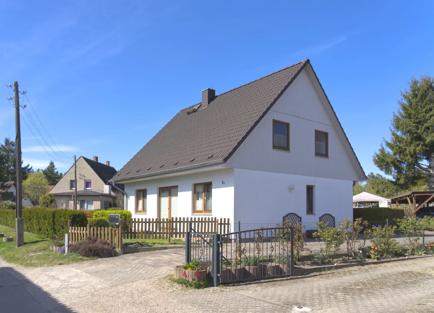 Two-story white house with a brown roof, a wooden fence, and a metal gate on a sunny day.