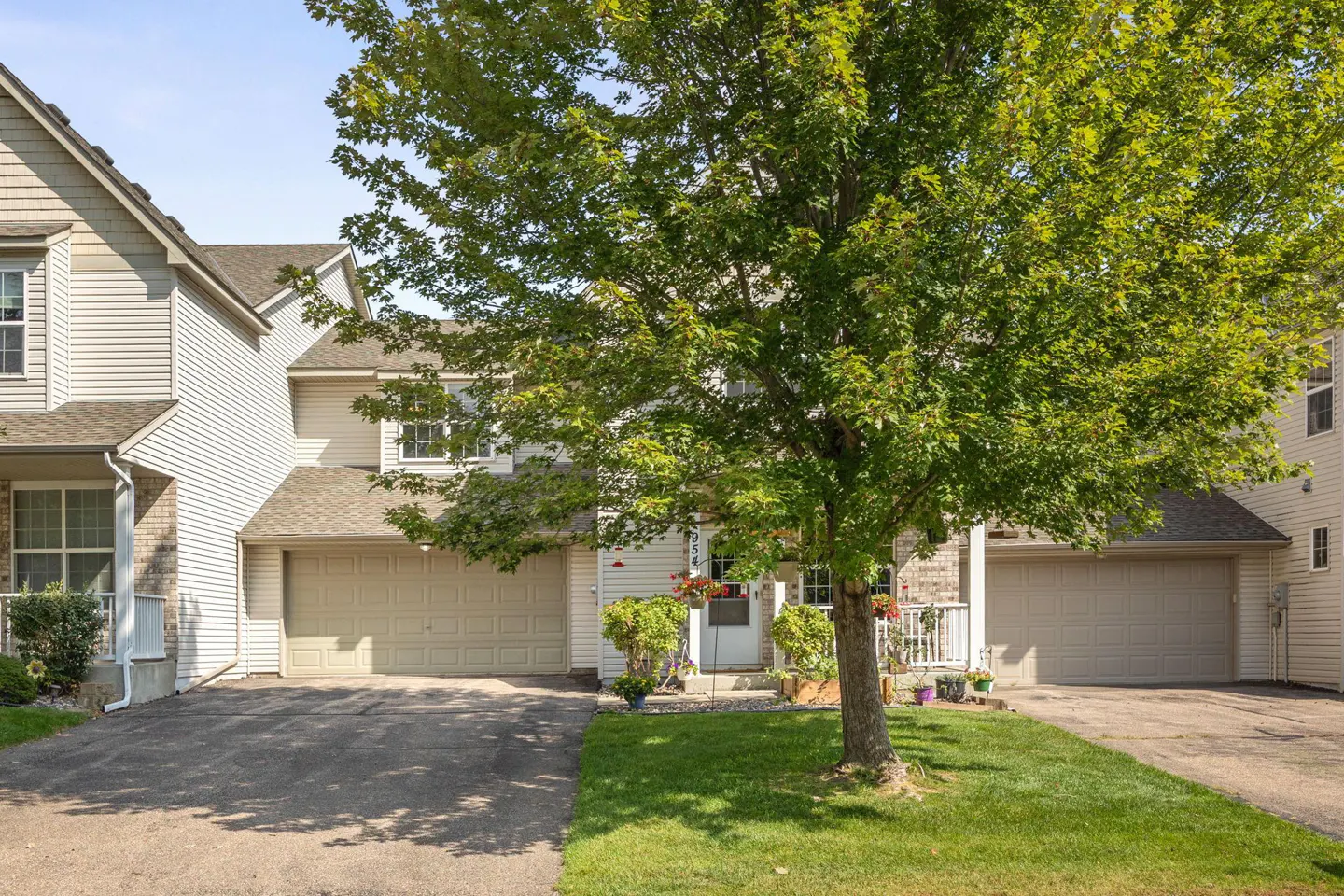 Exterior view of a two-story townhouse with a beige garage door and siding, a green lawn, and a large tree.