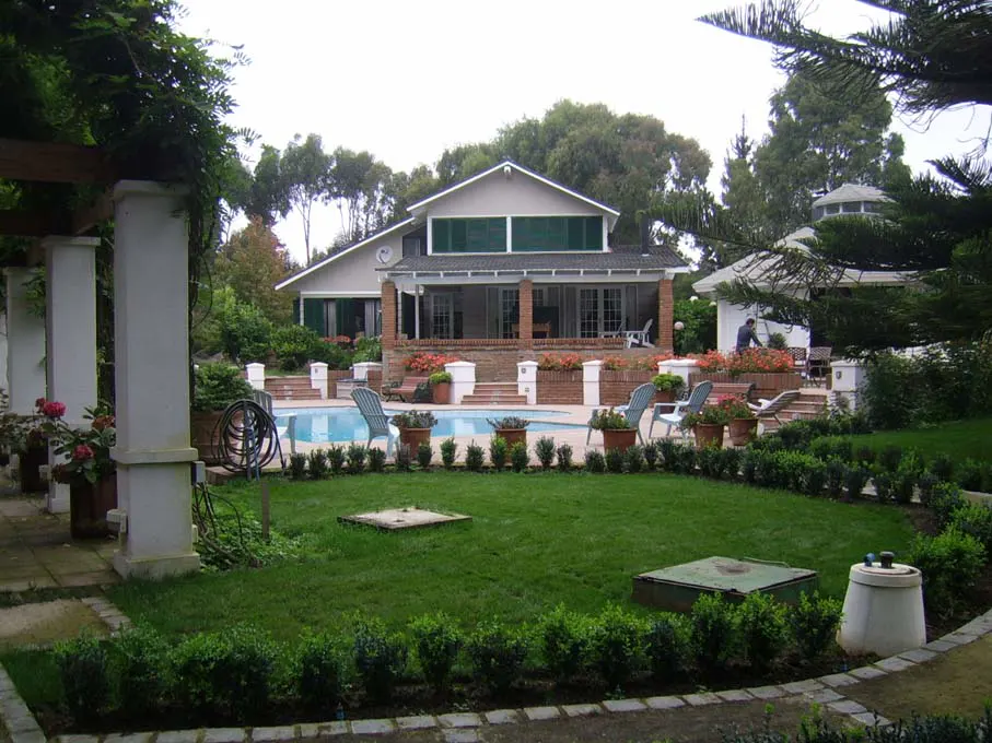 A backyard with a pool, green lawn, and a house with a brick porch.