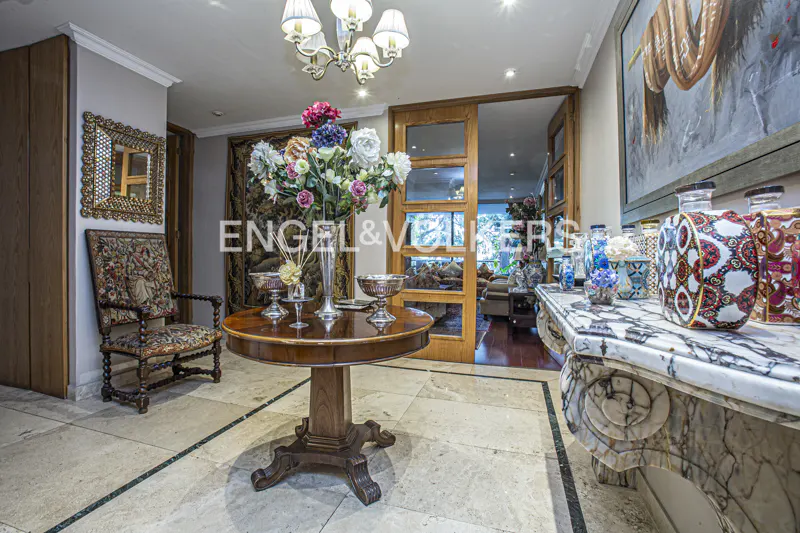 Elegant foyer with marble floors, a round wooden table with flowers, and a marble console table with decorative vases.