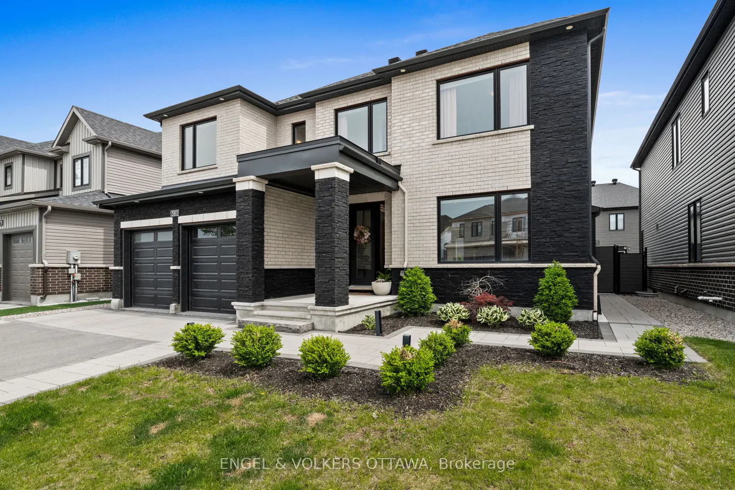 Modern two-story home with cream brick and black stone accents, a double garage, and a landscaped front yard.