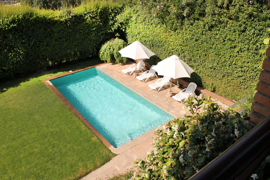 Aerial view of a rectangular pool with turquoise water, surrounded by green grass, lounge chairs, and white umbrellas.