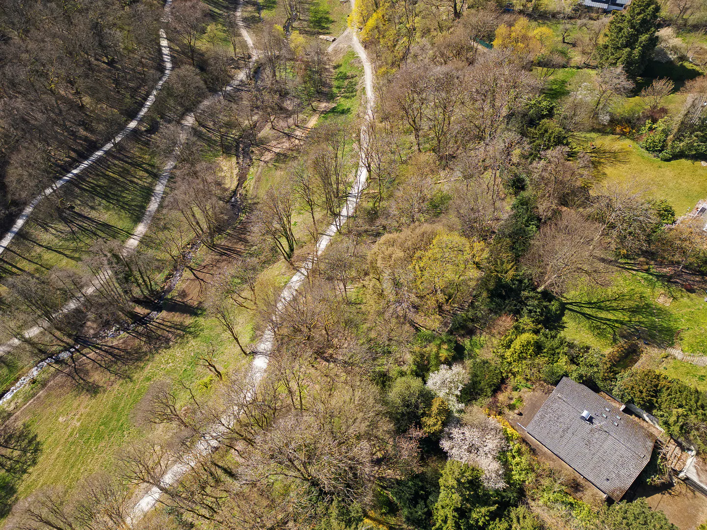 Aerial view of a property with a gray roof, surrounded by trees, green grass, and winding paths.