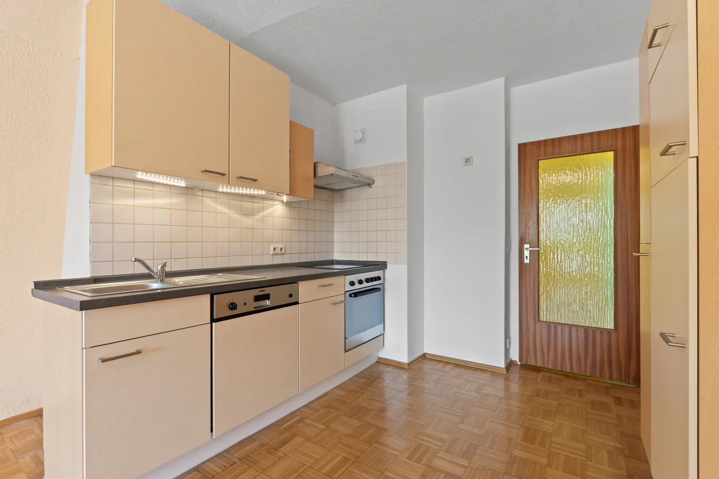 Kitchen with light wood cabinets, tiled backsplash, stainless steel appliances, and a wooden door with textured glass.
