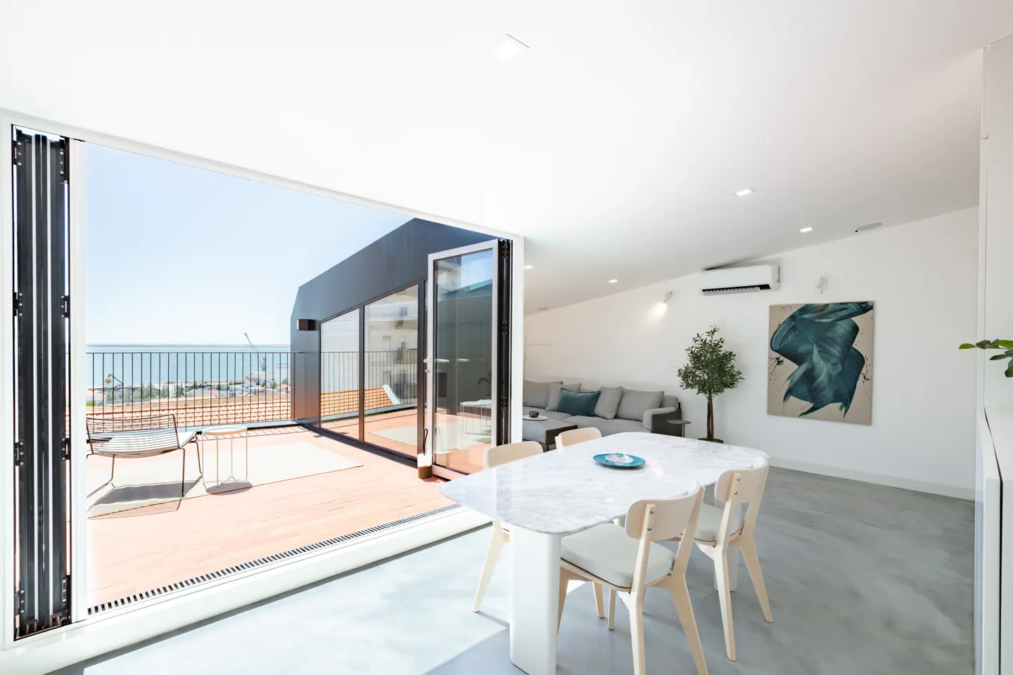 Modern dining area with marble table, opening to a sunny balcony with ocean views and outdoor seating.