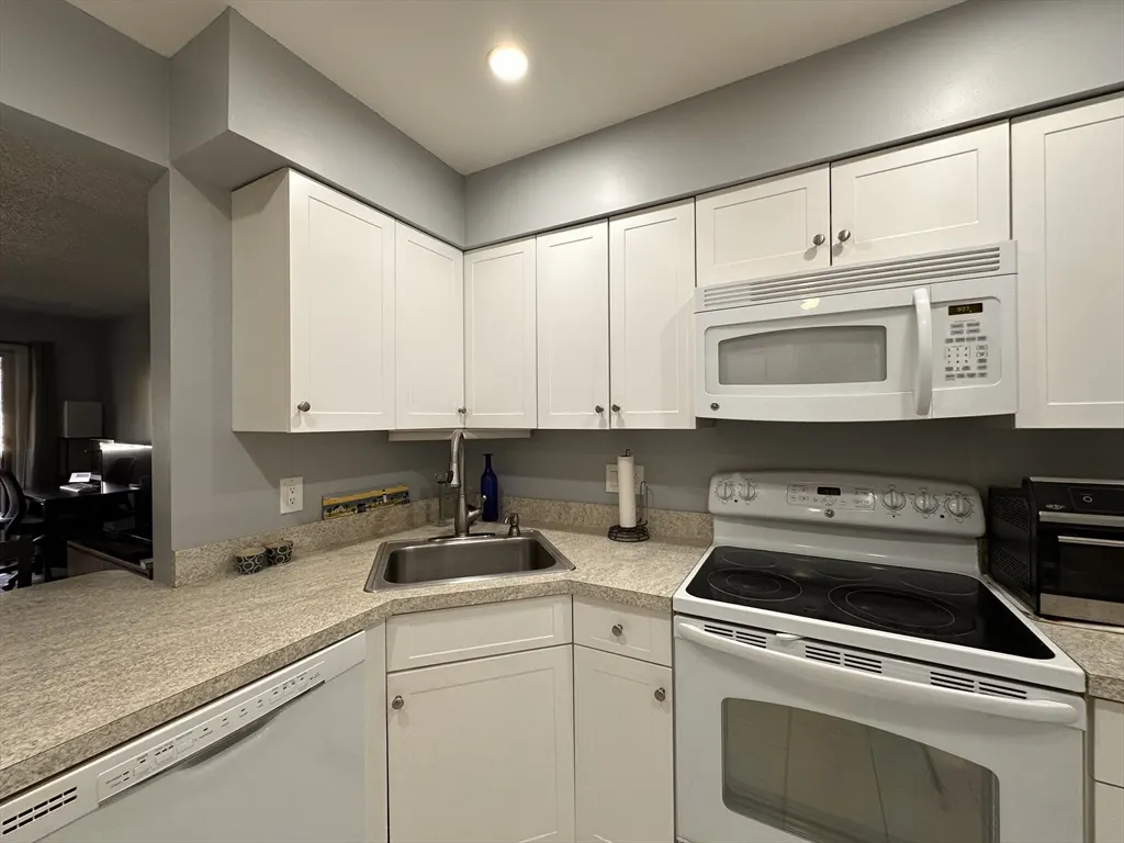 A kitchen with white cabinets, a stainless steel sink, and a white stove.