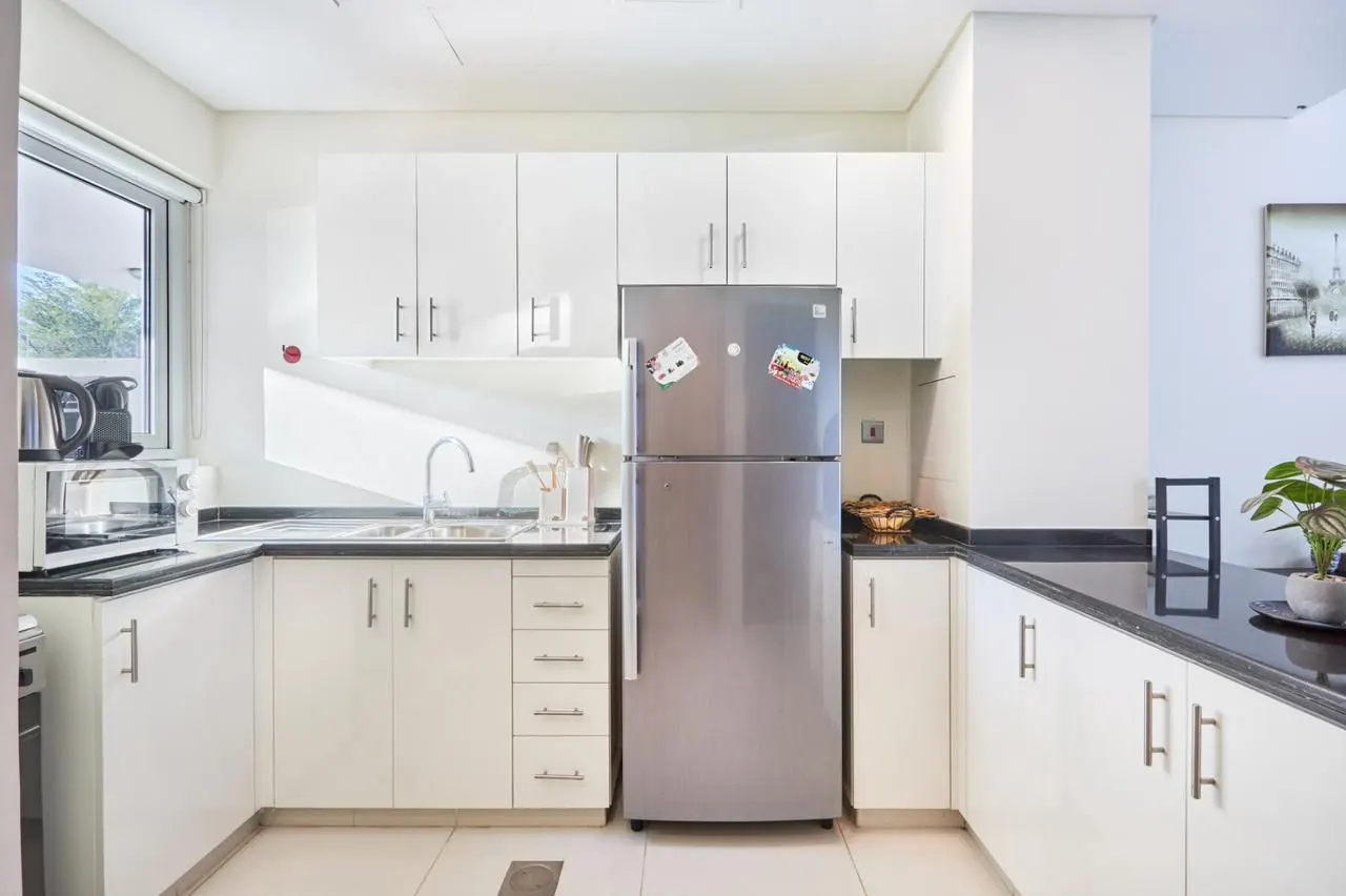 Bright kitchen with white cabinets, black countertops, and a stainless steel refrigerator. A window provides natural light.