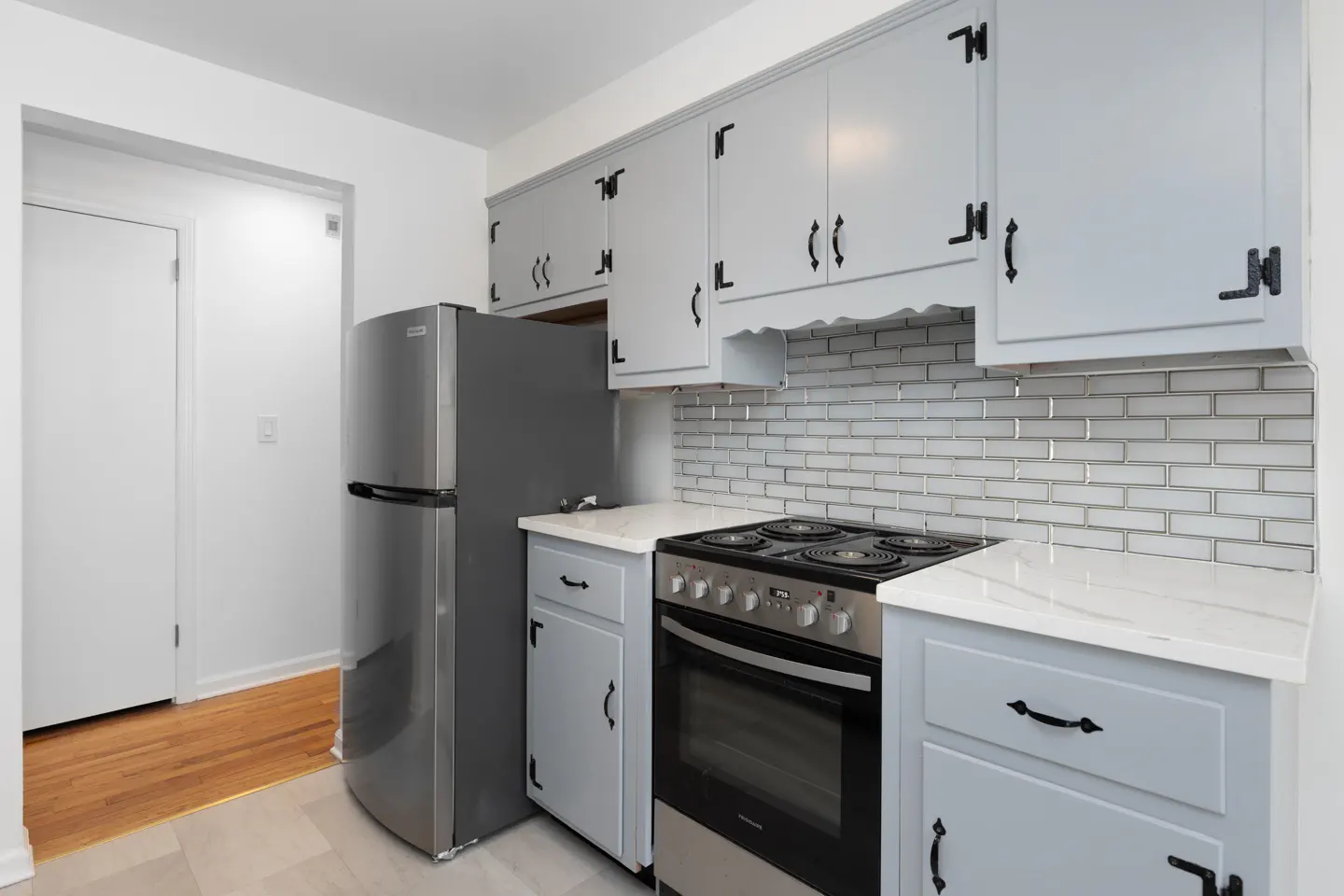A kitchen with gray cabinets, black hardware, stainless steel appliances, and white countertops.