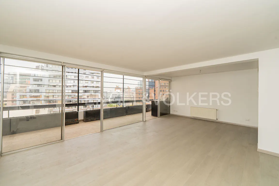 Bright, empty room with light wood floors and white walls. Large sliding glass doors open to a balcony with city views.