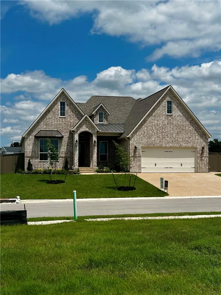 A single-story brick house with a gray roof, a two-car garage, and a green lawn under a blue sky.