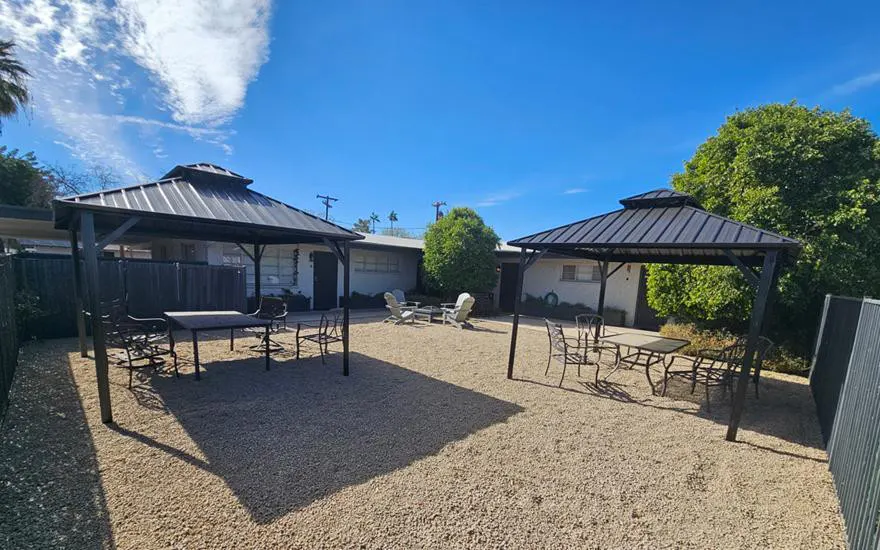 Outdoor courtyard with two black gazebos, gravel ground, and seating areas under a blue sky.